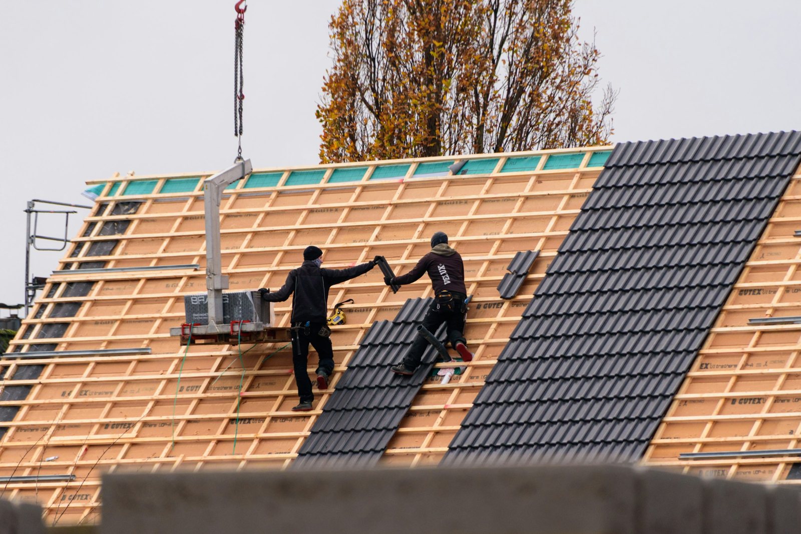 Twee dakdekkers leggen nieuwe dakpannen op een hellend dak